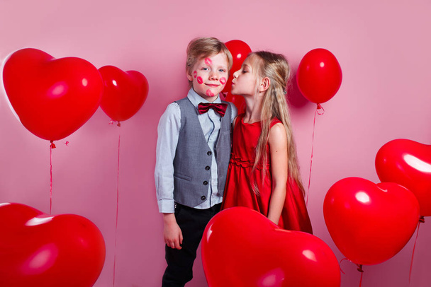 Funny little boy with red kisses on the skin and girl in red balloons in the shape of a heart - Foto, afbeelding
