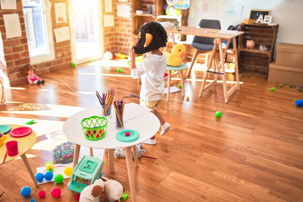 Hermosa rubia niño jugando con la máscara de mono de pie alrededor de un montón de juguetes en el jardín de infantes
 - Foto, imagen