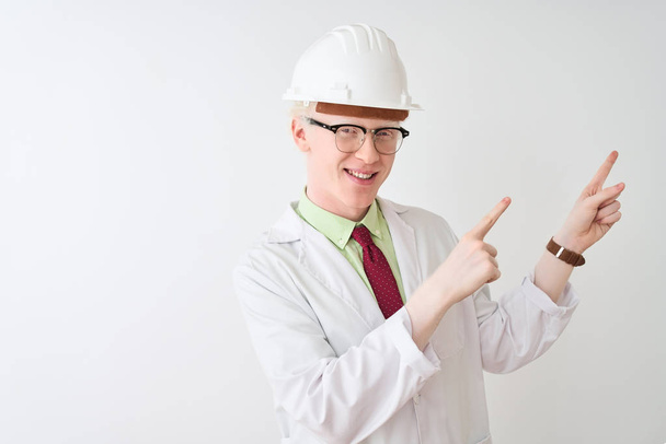 Albino wetenschapper man met bril en helm staande over geïsoleerde witte achtergrond glimlachend en kijkend naar de camera wijzend met twee handen en vingers naar de zijkant. - Foto, afbeelding