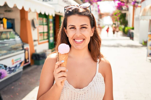 Young beautiful woman eating ice cream cone at palour on a sunny day of summer on holidays - Photo, Image