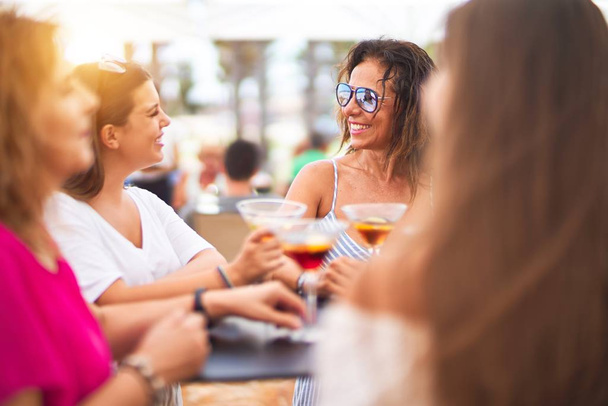 Beautiful group of women sitting at terrace of restaurant drinking cocktails speaking and smiling - Foto, Imagen