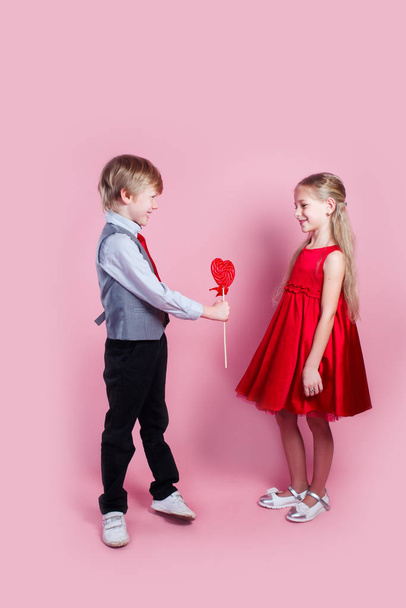 Funny boy and little girl with candy red lollipop in heart shape. Beautiful children eat sweets. Valentines day - Fotografie, Obrázek