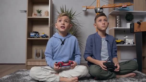 Close view of attractive two 10-12s boys which sitting on the carpet and playing video game using gamepads - Video