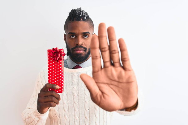 Uomo afroamericano con trecce in possesso di regalo di Natale su sfondo bianco isolato con mano aperta facendo segno di stop con espressione seria e sicura, gesto di difesa
 - Foto, immagini