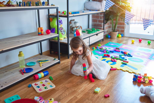 Adorable blonde toddler playing with building blocks around lots of toys at kindergarten - Photo, Image