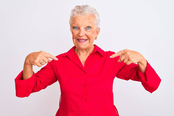 Donna anziana dai capelli grigi che indossa una camicia casual rossa in piedi su uno sfondo bianco isolato guardando fiducioso con il sorriso sul viso, puntandosi con le dita orgoglioso e felice
. - Foto, immagini