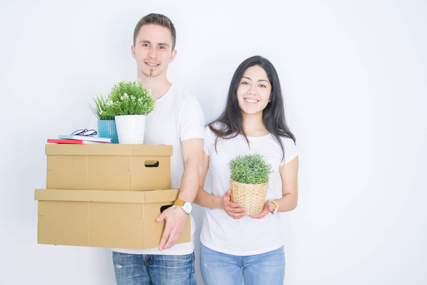 Young beautiful couple holding cardboard boxes standing over isolated white background with a happy face standing and smiling with a confident smile showing teeth - Photo, Image