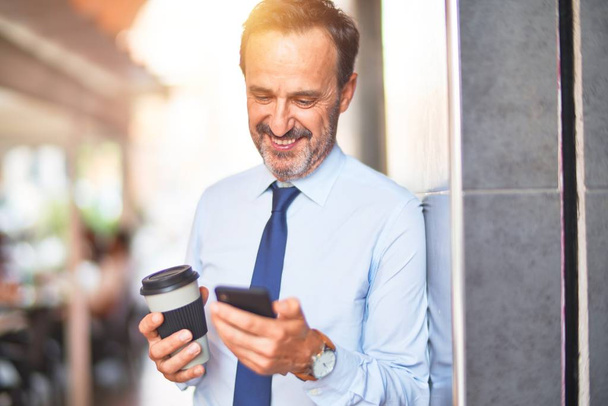 Keski-ikä komea liikemies älypuhelimen juominen vie pois kahvia hymyillen
 - Valokuva, kuva