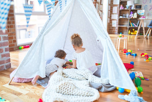 Beautiful toddlers playing inside tipi over blanket around lots of toys at kindergarten - 写真・画像