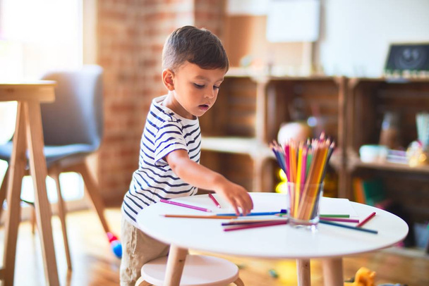 Beautiful toddler boy drawing cute draw using colored pencils at kindergarten - Fotó, kép
