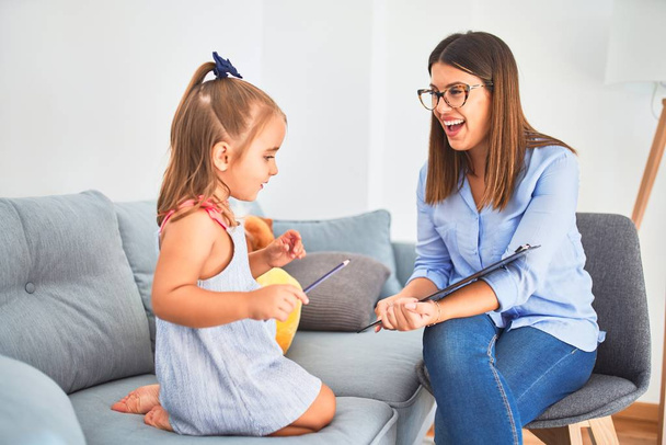 Fiatal terapeuta nő beszél és kezel gyermek, tanácsadó és viselkedés korrekció a pedagógus fizetőszobában jegyzetel a vágólapon - Fotó, kép