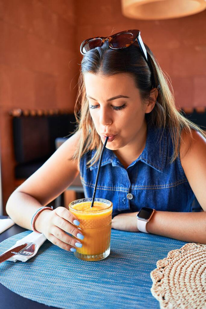 Young beautiful woman sitting at restaurant enjoying summer vacation drinking healthy smoothie - Fotó, kép