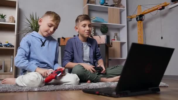 Side view of two handsome modern teen boys which sitting on the carpet and emotionally playing video game on computer using joysticks - Video