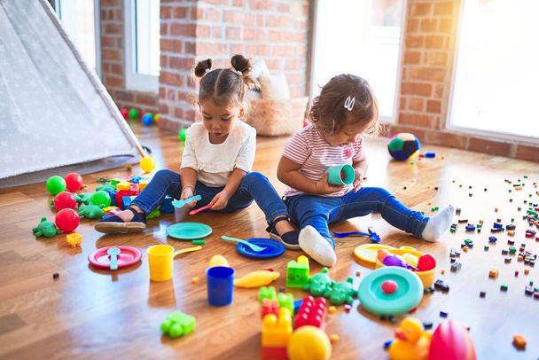 Suloiset pikkulapset, jotka pelaavat aterioita käyttämällä muovista ruokaa ja ruokailuvälineitä lelu päiväkodissa
 - Valokuva, kuva