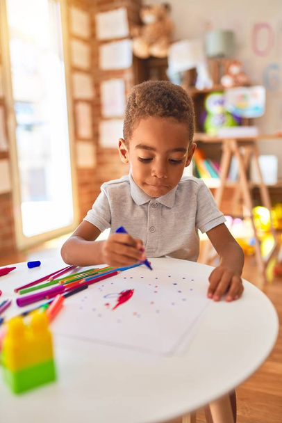 Güzel Afrikalı Amerikalı çocuk anaokulunda kağıt ve kalem kullanarak resim çiziyor. - Fotoğraf, Görsel