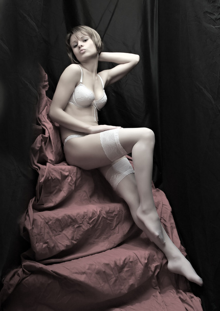 Chica coqueta sentada con largas piernas delgadas en medias de nylon blancas. Fotografía monocromática de bajo perfil
. - Foto, imagen