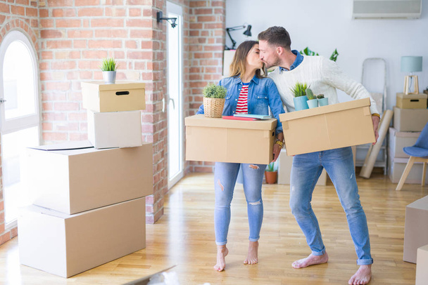 Young beautiful couple moving cardboard boxes and kissing at new home - Photo, Image