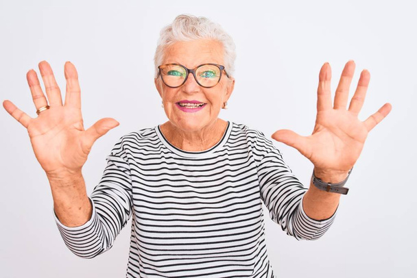 Senior grey-haired woman wearing striped navy t-shirt glasses over isolated white background showing and pointing up with fingers number ten while smiling confident and happy. - Photo, Image