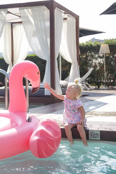 Adorable niña que se divierte día en la piscina y jugando con gran flamenco inflable rosa
 - Foto, imagen