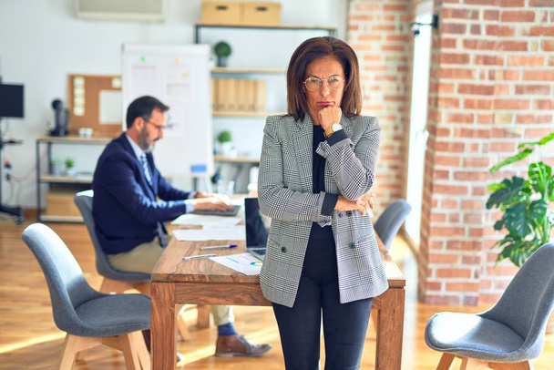 Middle age beautiful businesswoman wearing jacket and glasses standing at the office thinking looking tired and bored with depression problems with crossed arms. - Photo, Image