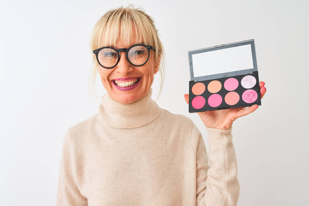 Middle age woman wearing sweater and glasses using makeup over isolated white background with a happy face standing and smiling with a confident smile showing teeth - Fotó, kép