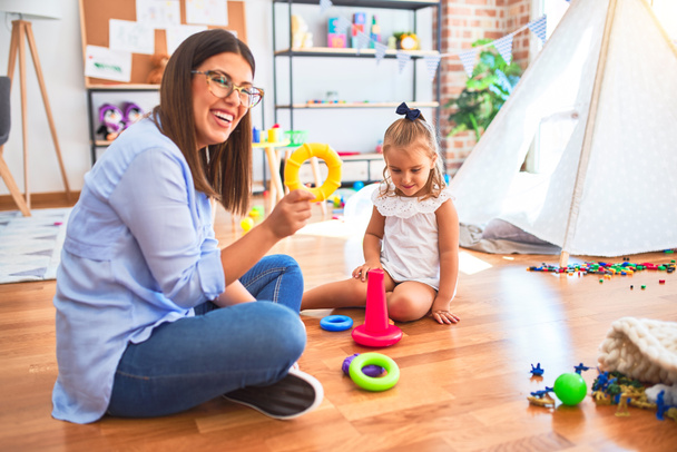 Caucasian girl kid playing and learning at playschool with female teacher. Mother and daughter at playroom playing with inteligence toys - Photo, Image