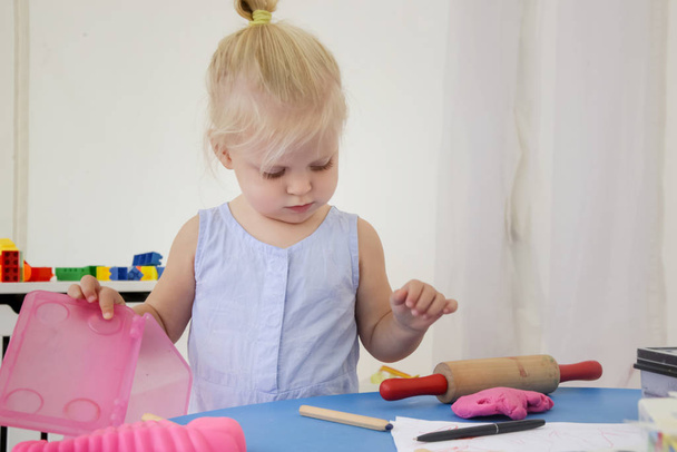 Peuter meisje spelen met modelleren klei. Speeldeeg stelt kinderen in staat om fijne motorische vaardigheden te ontwikkelen, vingers, handen en polsen te versterken en natuurlijk nieuwsgierig te zijn en de wereld te verkennen met behulp van hun zintuigen - Foto, afbeelding