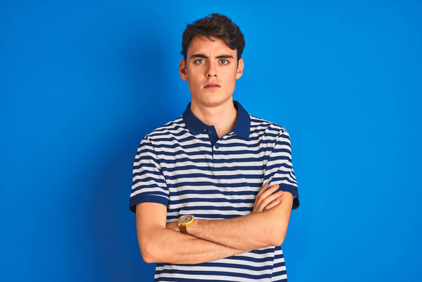 Tinédzser fiú alkalmi pólóban áll kék elszigetelt háttér szkeptikus és ideges, rosszalló kifejezés az arcon keresztbe tett karokkal. Negatív személy. - Fotó, kép