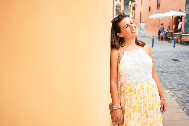 Menina bonita inclinada na parede laranja, jovem mulher amigável sorrindo feliz em um dia ensolarado de verão
 - Foto, Imagem