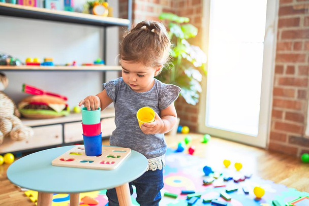 Όμορφο παιδί στέκεται παίζοντας με πολύχρωμα πλαστικά ποτήρια στο νηπιαγωγείο - Φωτογραφία, εικόνα