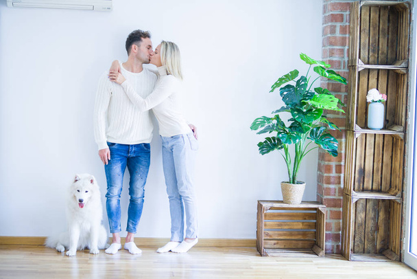 Young beautiful couple with dog kissing standing at new home - Foto, afbeelding