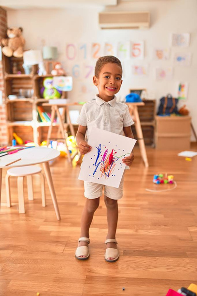 Bela criança afro-americana de pé segurando desenhar sorrindo no jardim de infância
 - Foto, Imagem