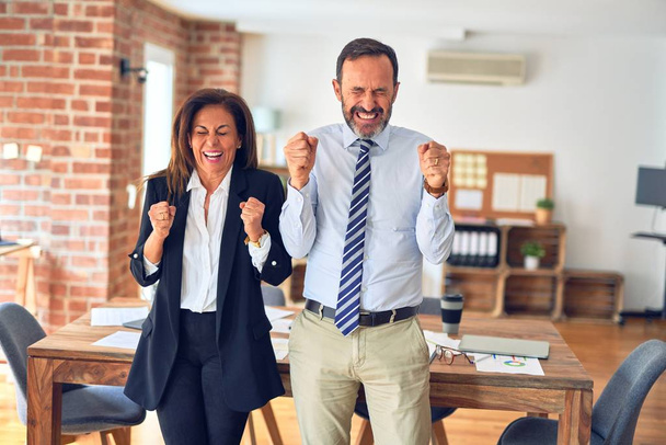 Двоє бізнесменів середнього віку, які працюють разом на зустрічі в офісі, захоплені успіхом з піднятими руками і закритими очима, святкуючи перемогу посміхаючись. концепція переможця
. - Фото, зображення