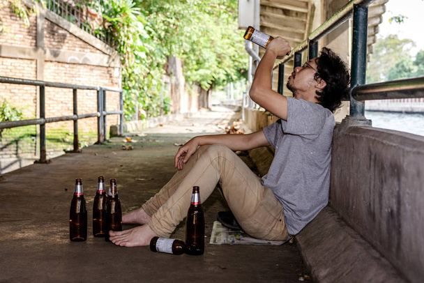 Retrato de um bêbado sentado olhando para as garrafas vazias de l
 - Foto, Imagem