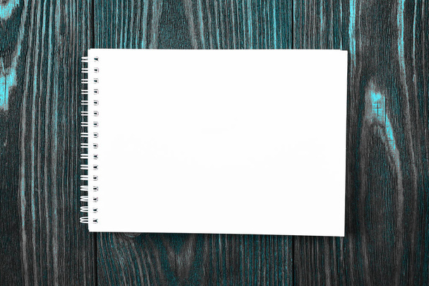 λευκό γραφείο Notepad βρίσκεται σε ένα φωτεινό μπλε χρώμα ξύλινο υπόβαθρο, μινιμαλιστικό σχεδιασμό, κορυφαία άποψη, επίπεδη lay, αντίγραφο χώρου - Φωτογραφία, εικόνα