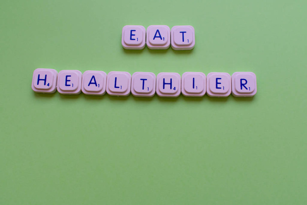 Lema motivacional: Come más sano, sobre un fondo verde hecho con letras de juego
 - Foto, imagen