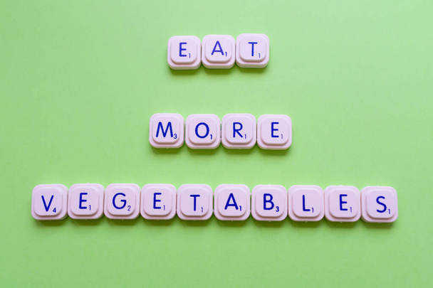 Slogan motivacional: Coma mais legumes, sobre um fundo verde feito com letras de jogo
 - Foto, Imagem