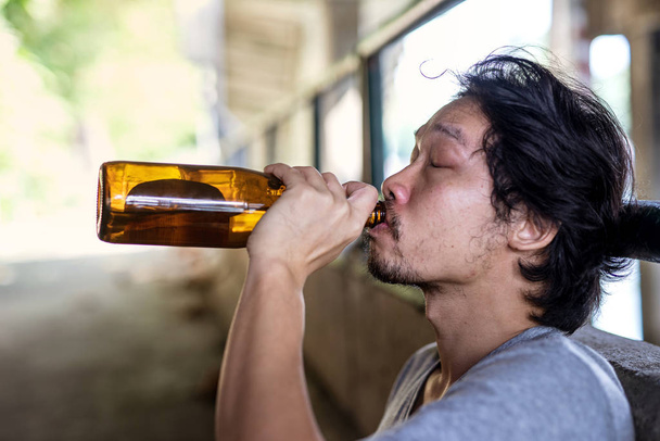 ポートレート酔った男が酒を飲むために瓶を拾う. - 写真・画像