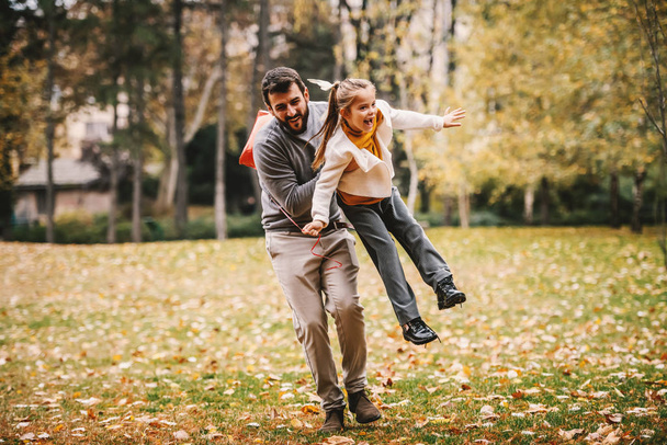 Leikkisä huolehtiva isä juoksee ja nostaa tyttärensä puistossa. Tyttö pitelee ilmapalloa ja nauraa. Laadukas perheaika
. - Valokuva, kuva