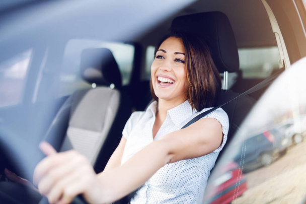 Morena caucasiana sorridente atraente dirigindo seu carro. As mãos estão no volante
. - Foto, Imagem