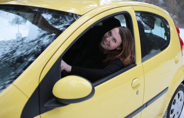 Gyönyörű vonzó lány zöld szemekkel és ruf haj egy sárga autó egy téli havas erdőben - Fotó, kép