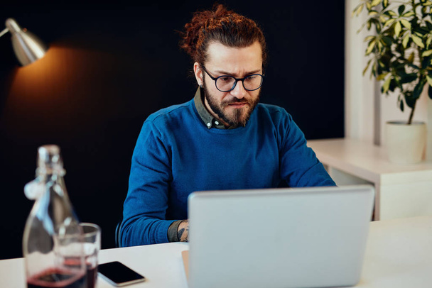 Jóképű fehér szakállas üzletember ül a modern irodájában, és laptopot használ a jelentés írásához.. - Fotó, kép