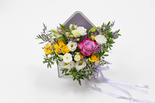 bright fresh composition of fresh flowers (colors: white, pink, purple) (flowers: rose, eustoma, lily, carnation) in a gift box in the form of an envelope on a white background - Photo, image