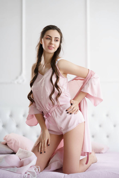 Mulher bonita sorrindo sensualmente na cama brincando com seu conjunto de pijama rosa
 - Foto, Imagem