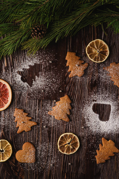 クリスマスのモミの木とハートの形でジンジャーブレッドクッキー、木製の背景に粉砂糖、柑橘類乾燥果物、モミの木の枝、トップビュー - 写真・画像
