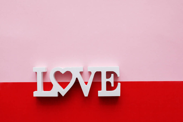 Słowo miłość składa się z drewnianych liter umieszczonych na różowym i czerwonym tle. Kartka okolicznościowa Walentynki i Dzień Kobiet - Zdjęcie, obraz