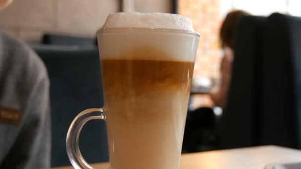 Lahodné čerstvě uvařené latté na stole v kavárně. Mléčná pěna z latté kávy v průhledném dlouhém speciálním skle. Káva sediment mísí a dělá neobvyklé vzory - Záběry, video