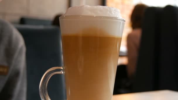 Lahodné čerstvě uvařené latté na stole v kavárně. Mléčná pěna z latté kávy v průhledném dlouhém speciálním skle. Káva sediment mísí a dělá neobvyklé vzory - Záběry, video