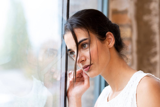 Portrait of a beautiful young woman standing at a window - Foto, imagen