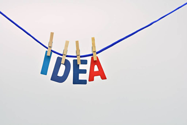 The word idea made with wooden letters hanging on a rope with clothespins, and a light bulb - Foto, Imagen